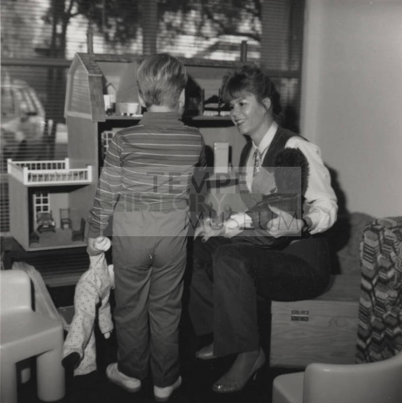 Woman entertains young boy with dolls and dollhouse