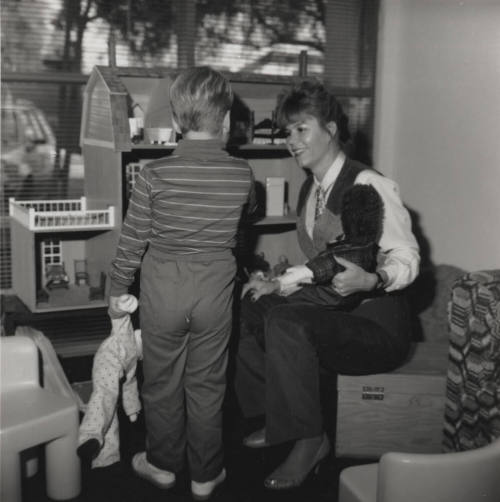 Woman entertains young boy with dolls and dollhouse