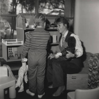 Woman entertains young boy with dolls and dollhouse
