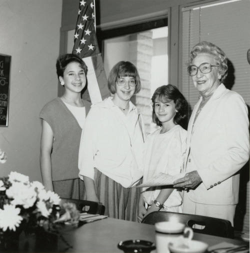 Four Females stand in front of a U.S. Flag