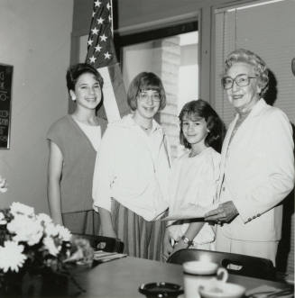 Four Females stand in front of a U.S. Flag