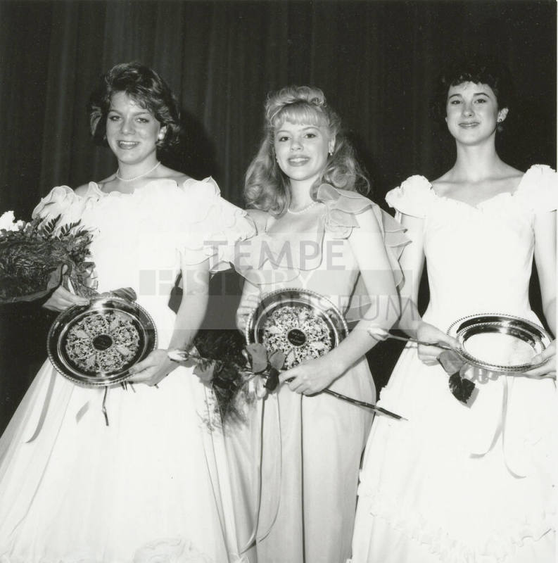 Three standing females wearing ballgowns each hold a bouquet and plate