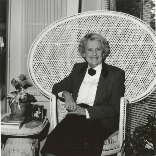 Older woman sits in living room in woven chair