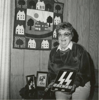 Woman poses in home with quilt and SS Dachau sign