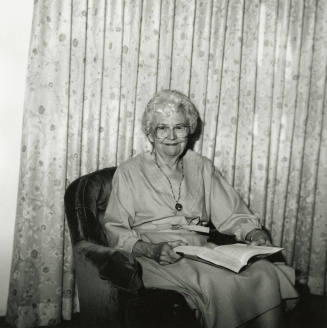 Unidentified Gray-Haired Woman Sits in Chair with Book