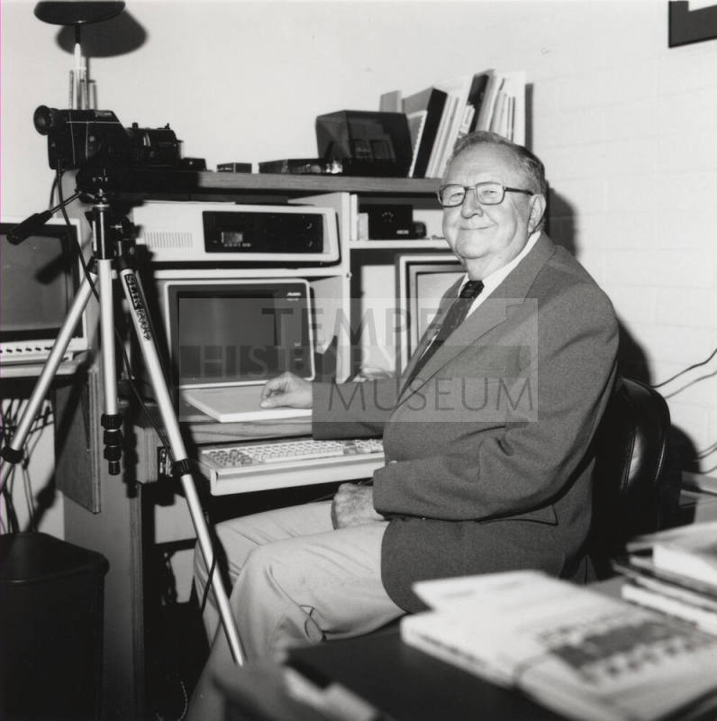 Unidentified Man with Glasses & a Smile Sits in well-equipped Office