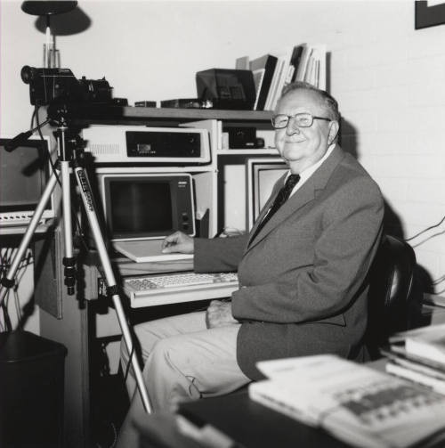 Unidentified Man with Glasses & a Smile Sits in well-equipped Office