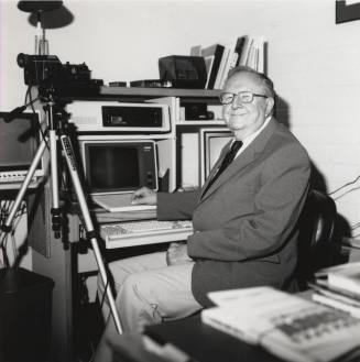 Unidentified Man with Glasses & a Smile Sits in well-equipped Office