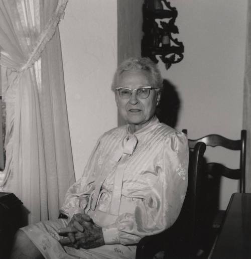 Unidentified Older woman sits in a chair in her home