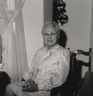 Unidentified Older woman sits in a chair in her home