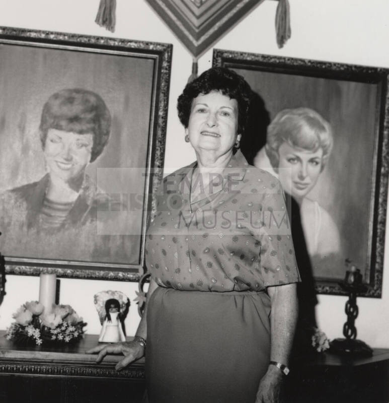 Unidentified woman poses in front of two painted portraits of women