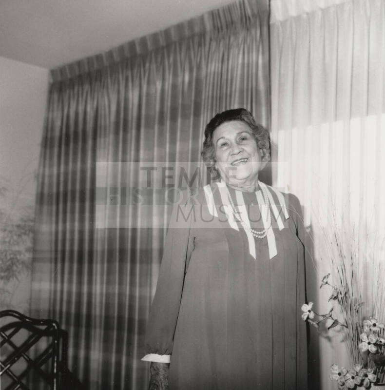 Unidentified woman poses in front of living room flowers & drapes (1 of 2)