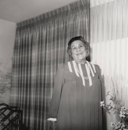 Unidentified woman poses in front of living room flowers & drapes (1 of 2)