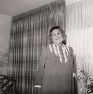 Unidentified woman poses in front of living room flowers & drapes (1 of 2)