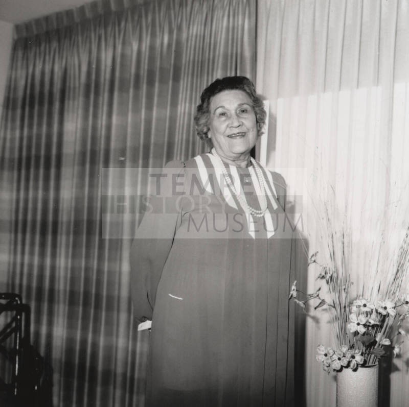Unidentified woman poses in front of living room flowers & drapes (2 of 2)