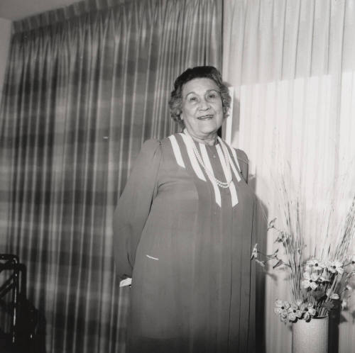 Unidentified woman poses in front of living room flowers & drapes (2 of 2)