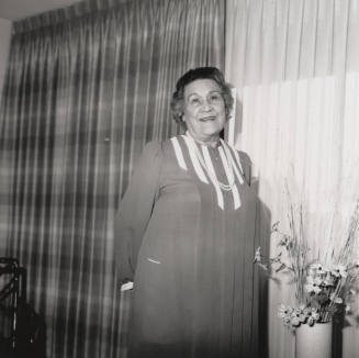 Unidentified woman poses in front of living room flowers & drapes (2 of 2)