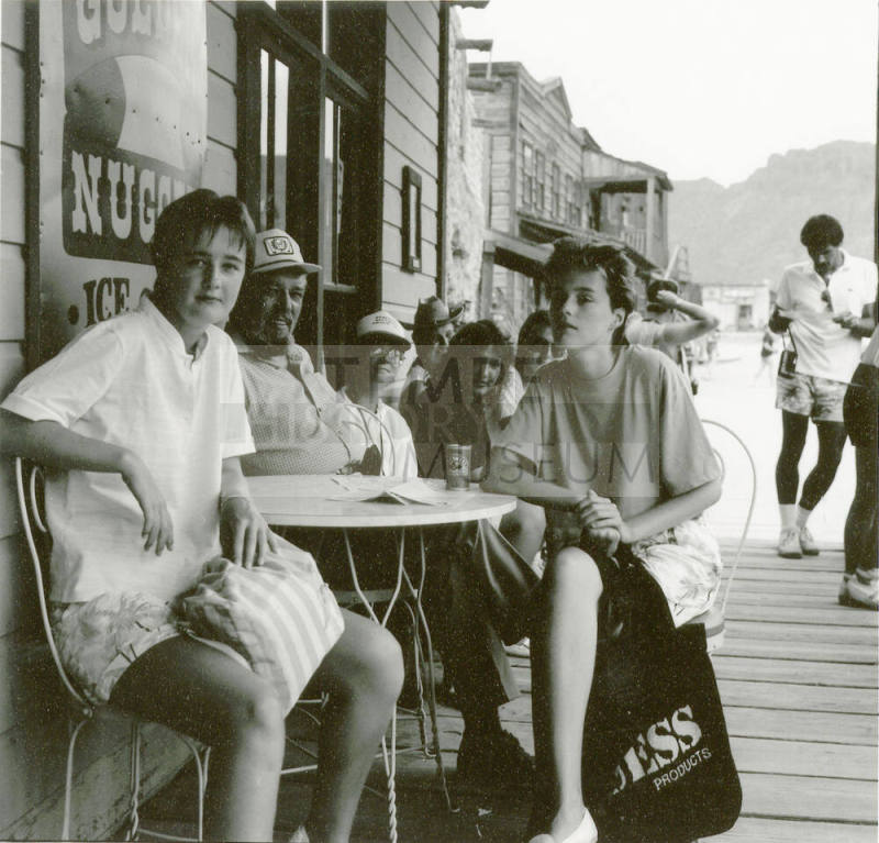 A group of people sit outside around a table posing for a picture