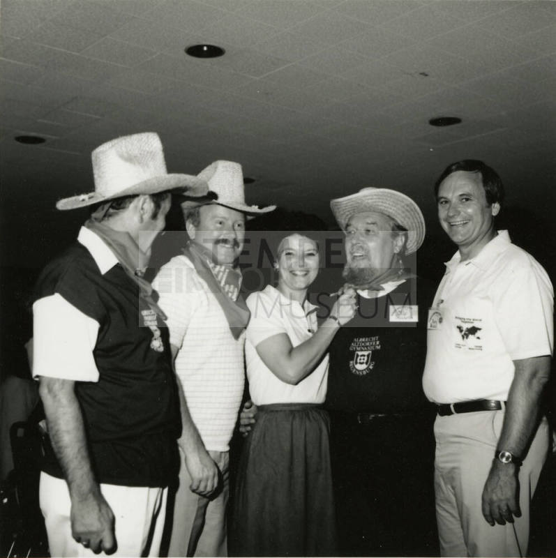 Three unknown men dressed in cowboy regalia stand with a woman and Harry Mitchell (on the right)