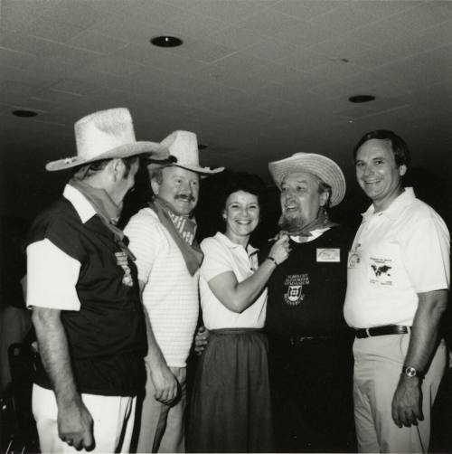 Three unknown men dressed in cowboy regalia stand with a woman and Harry Mitchell (on the right)