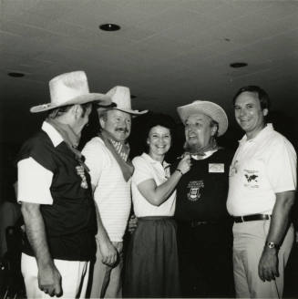 Three unknown men dressed in cowboy regalia stand with a woman and Harry Mitchell (on the right)