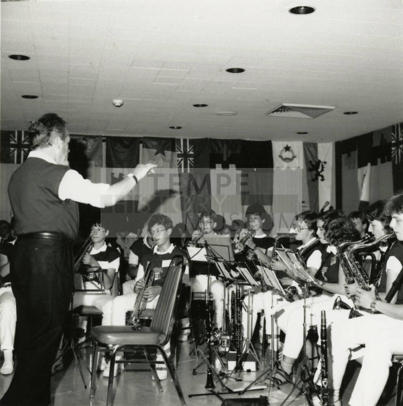 Conductor leads a band of primarily woodwind and brass instruments