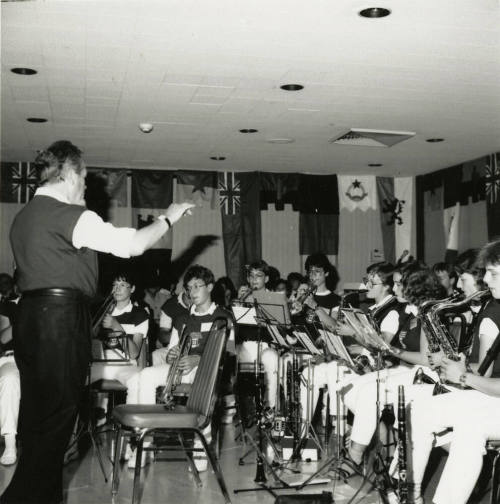 Conductor leads a band of primarily woodwind and brass instruments