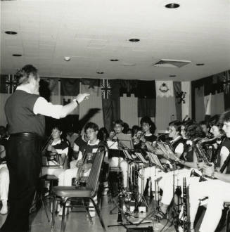 Conductor leads a band of primarily woodwind and brass instruments