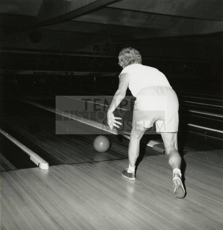 An unknown woman rolls a bowling ball down a lane at a bowling alley