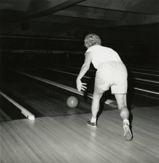 An unknown woman rolls a bowling ball down a lane at a bowling alley