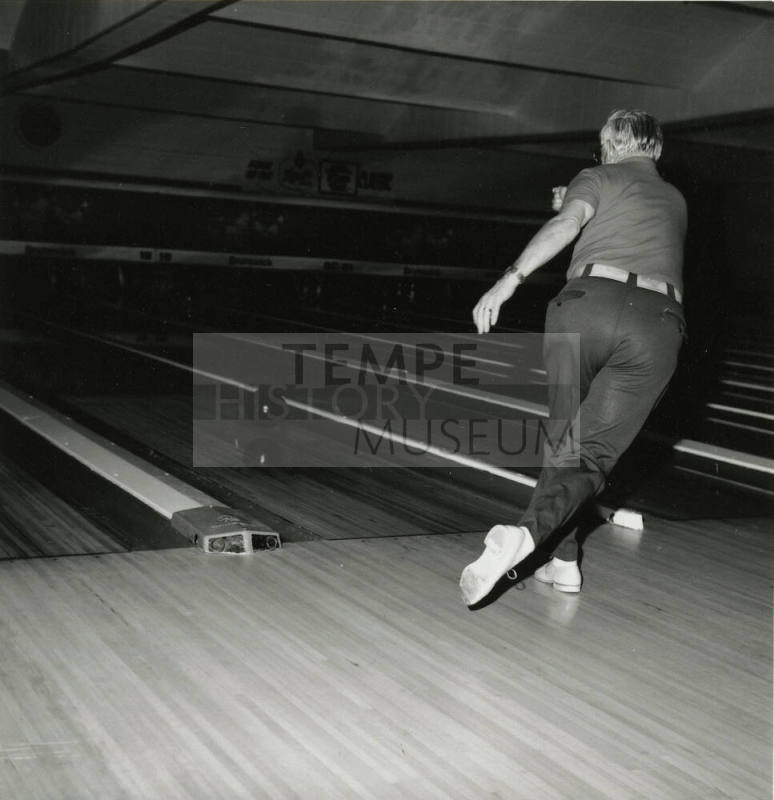 An unknown man rolls a bowling ball down a lane at a bowling alley.