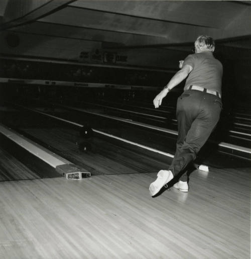 An unknown man rolls a bowling ball down a lane at a bowling alley.