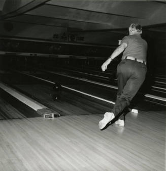 An unknown man rolls a bowling ball down a lane at a bowling alley.