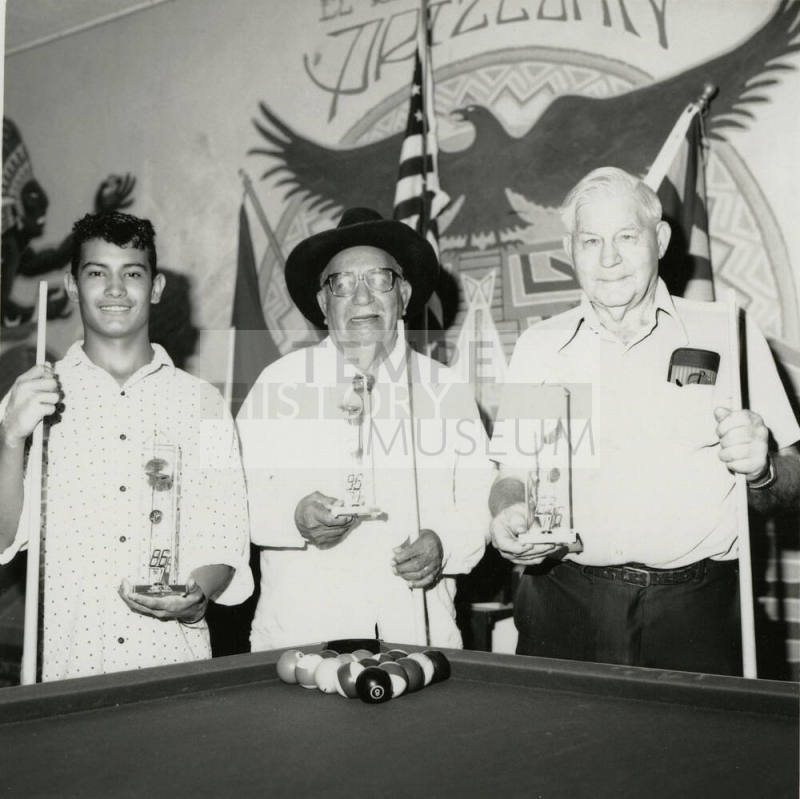 Three unidentified men at a pool table with trophies