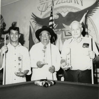 Three unidentified men at a pool table with trophies