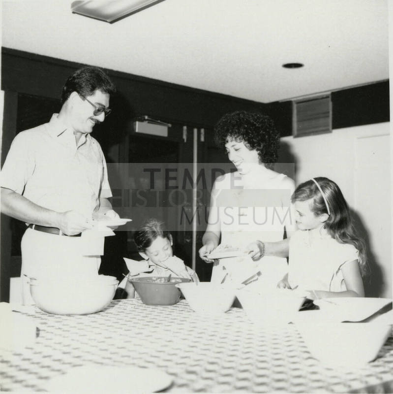 Unidentified family standing at a table sampling food