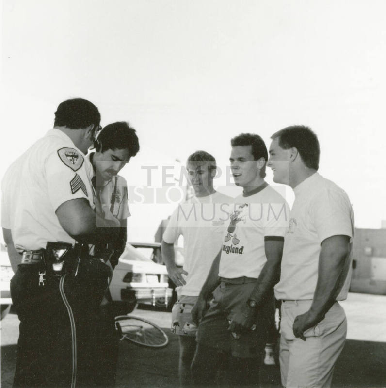 Three young men and two police officers stand outside in a parking lot