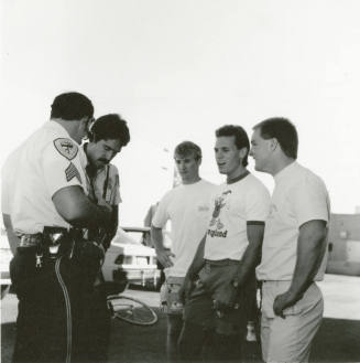 Three young men and two police officers stand outside in a parking lot