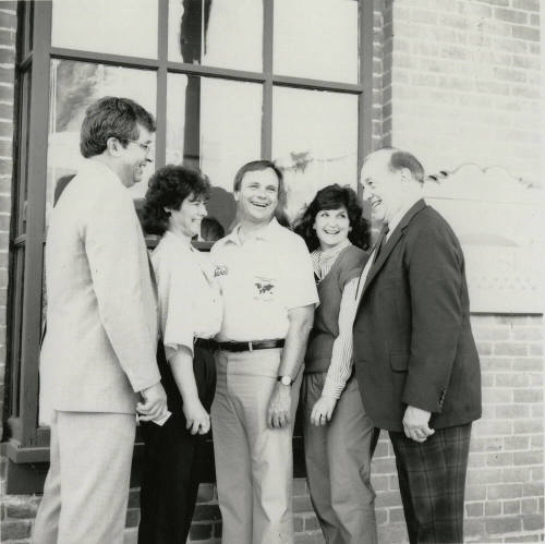Three unidentified people, Harry Mitchell (center), and Richard Neuheisel (left) outside the Hackett House