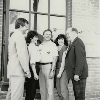 Three unidentified people, Harry Mitchell (center), and Richard Neuheisel (left) outside the Hackett House