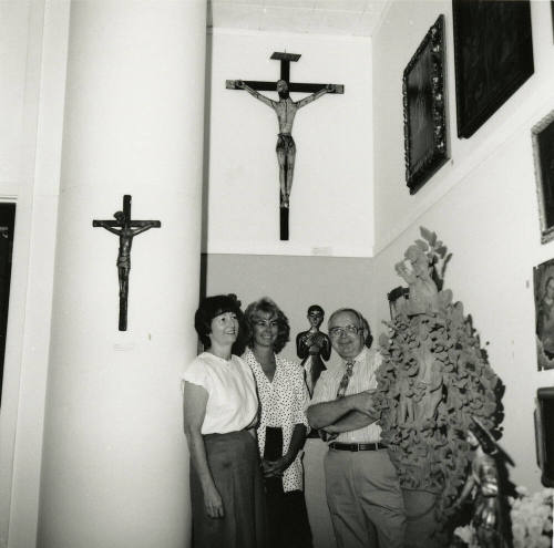 Three unidentified people stand amongst a religious art display