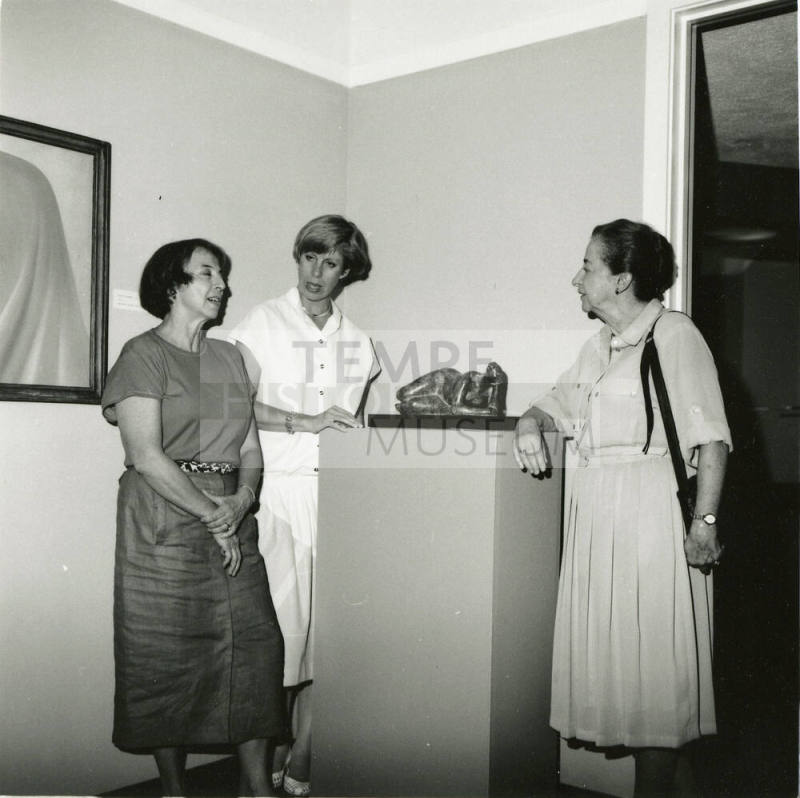 Three unidentified women gather around a sculpture.