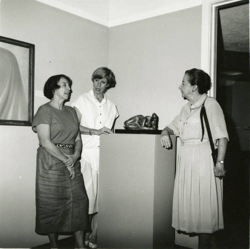 Three unidentified women gather around a sculpture.