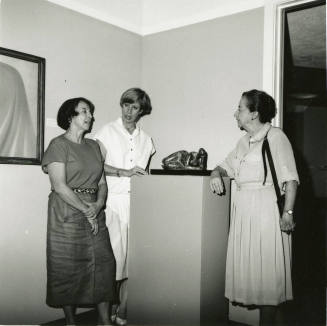 Three unidentified women gather around a sculpture.
