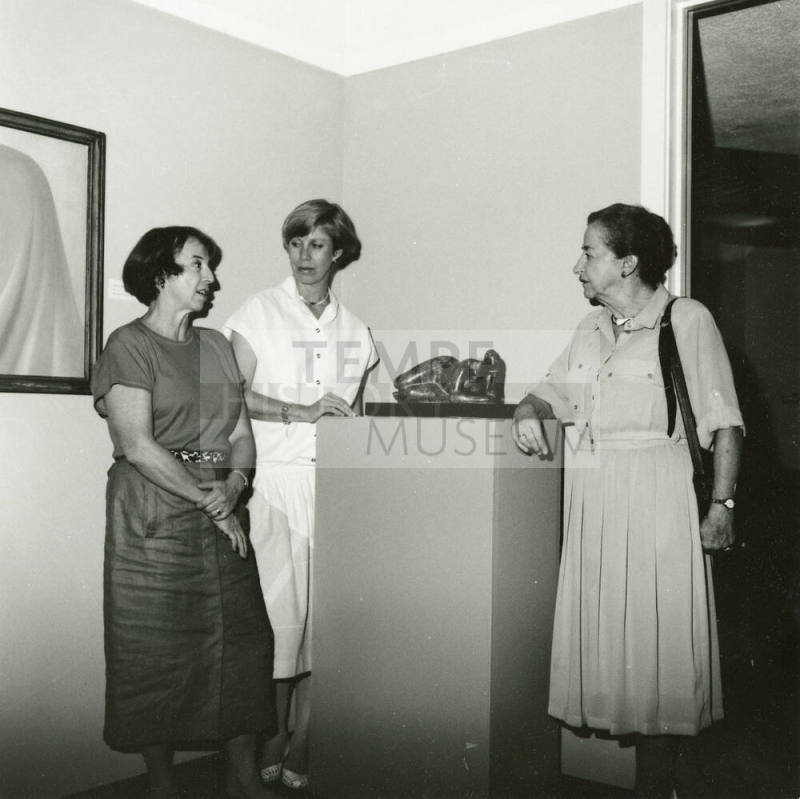 Three unidentified women gather around a sculpture at an art exhibit