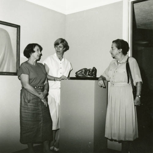Three unidentified women gather around a sculpture at an art exhibit