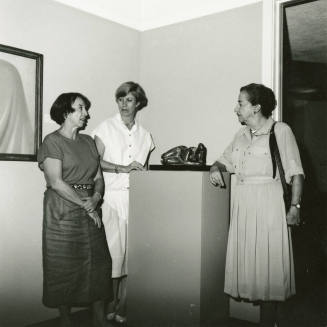 Three unidentified women gather around a sculpture at an art exhibit