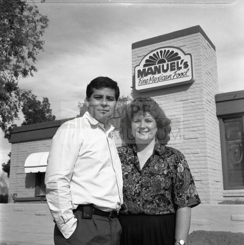 David and Pamela Salazar 27th year of Manuel's Restaurant, standing outside with the sign above their heads
