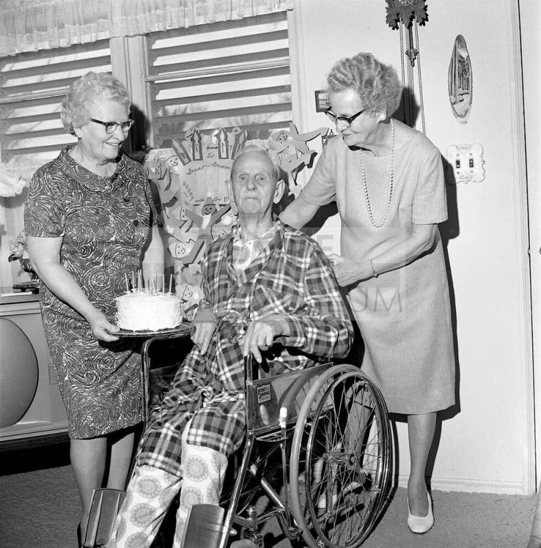 Two women give a man in a wheelchair a birthday cake