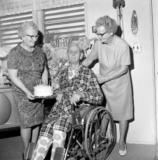 Two women give a man in a wheelchair a birthday cake